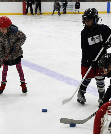 young children on ice with sticks and pucks